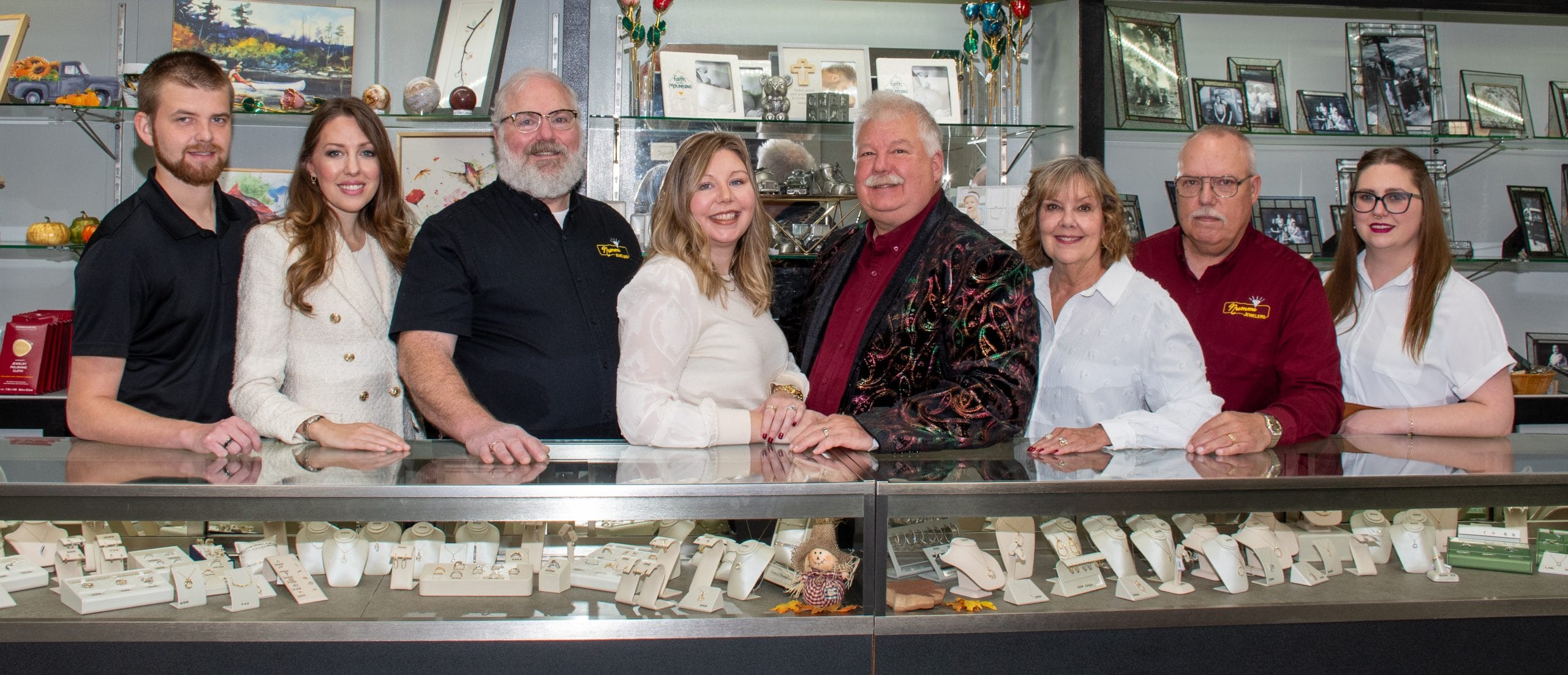 The Nummi Jewelers team, eight people, standing behind the glass jewelry cases in the Superior store